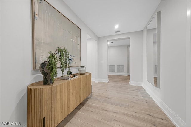 corridor with light wood-type flooring, baseboards, and visible vents