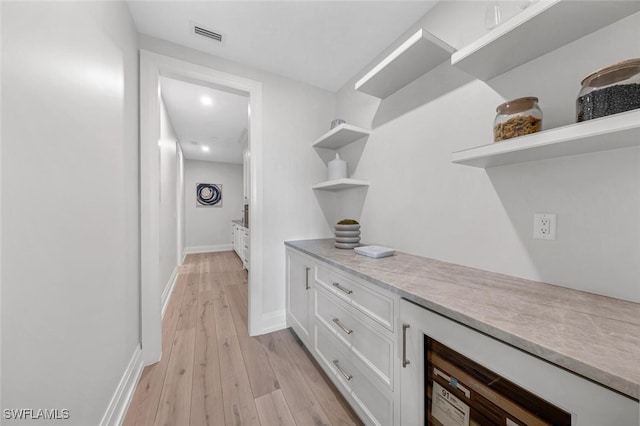 corridor featuring visible vents, light wood-style flooring, and baseboards