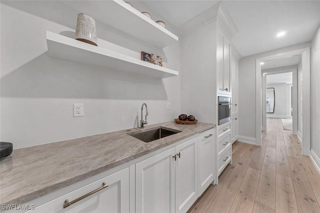 kitchen with light wood finished floors, white cabinets, oven, open shelves, and a sink