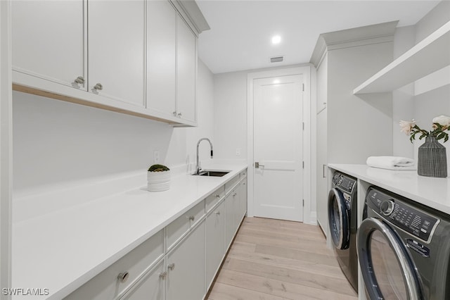 washroom featuring cabinet space, visible vents, light wood-type flooring, washing machine and dryer, and a sink