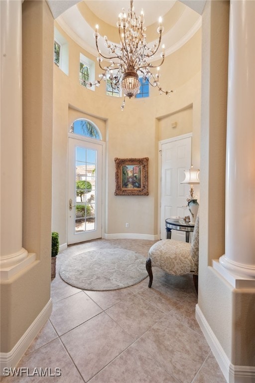 entryway featuring light tile patterned floors, a chandelier, ornate columns, a tray ceiling, and a high ceiling