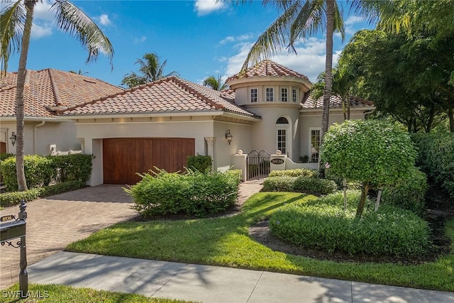 mediterranean / spanish home with a gate, an attached garage, stucco siding, a tile roof, and decorative driveway