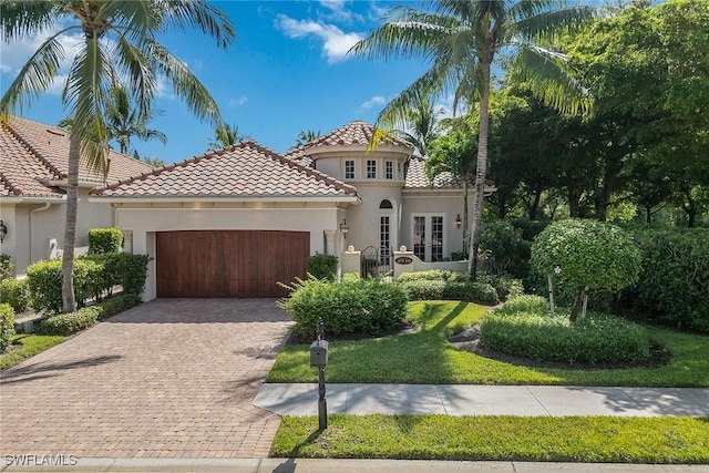 mediterranean / spanish house with a tile roof, stucco siding, french doors, decorative driveway, and an attached garage