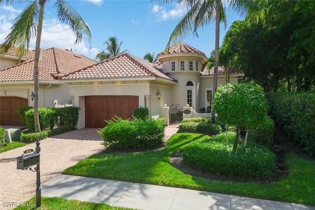 mediterranean / spanish-style home featuring a tiled roof, stucco siding, decorative driveway, a garage, and a gate