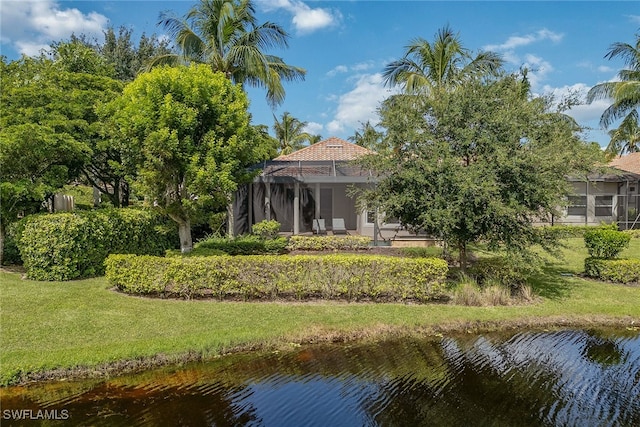 back of house with glass enclosure, a yard, and a water view