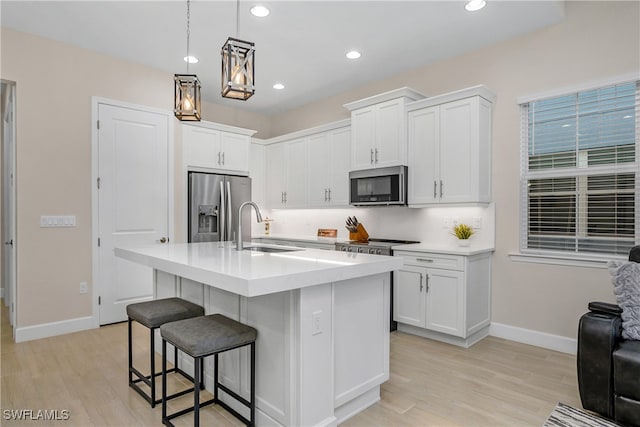 kitchen with appliances with stainless steel finishes, sink, a center island with sink, white cabinets, and light hardwood / wood-style floors