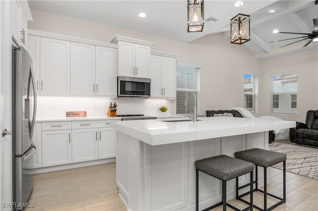 kitchen with a kitchen island with sink, white cabinets, appliances with stainless steel finishes, decorative light fixtures, and light hardwood / wood-style floors