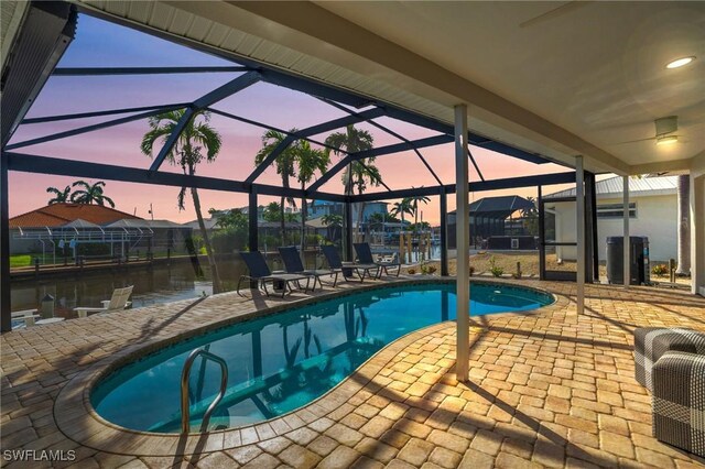 pool at dusk featuring a lanai, a patio area, and a water view