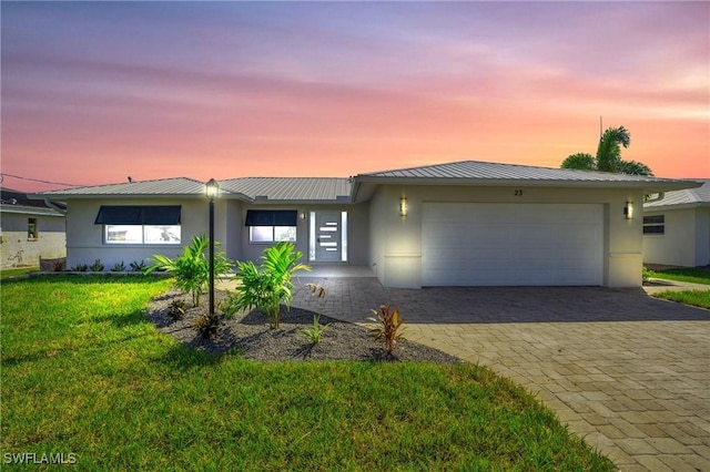 view of front of house with metal roof, an attached garage, decorative driveway, a lawn, and stucco siding