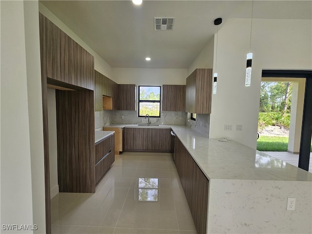 kitchen featuring light stone counters, kitchen peninsula, decorative light fixtures, decorative backsplash, and light tile patterned flooring