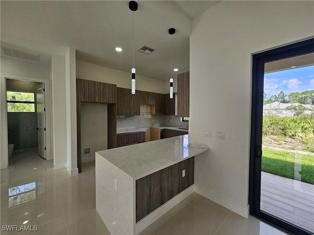 kitchen featuring kitchen peninsula, decorative backsplash, decorative light fixtures, and light tile patterned flooring