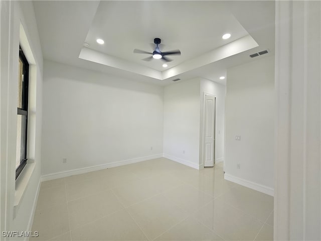 tiled empty room featuring a raised ceiling and ceiling fan