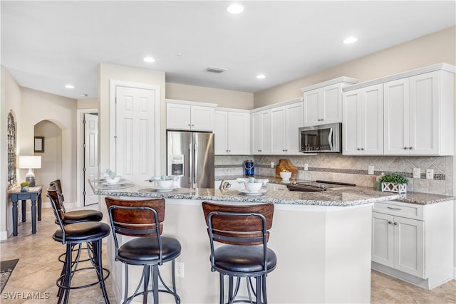 kitchen featuring stainless steel appliances, white cabinets, decorative backsplash, and light stone counters