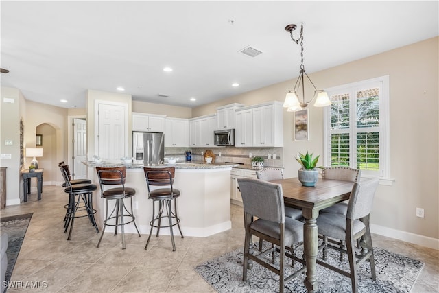 kitchen featuring stainless steel appliances, light stone counters, hanging light fixtures, backsplash, and white cabinetry