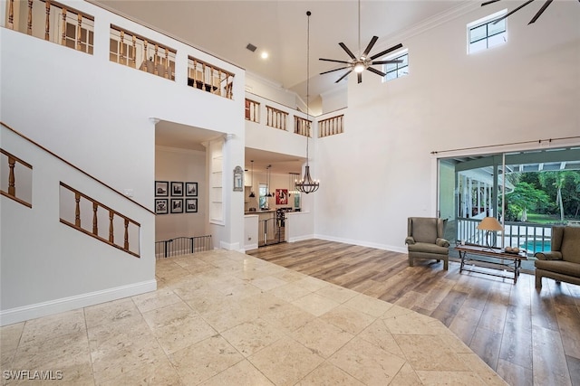 foyer with ceiling fan with notable chandelier, ornamental molding, wood-type flooring, and a high ceiling