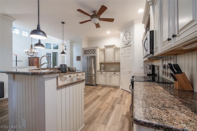 kitchen with dark stone countertops, ceiling fan with notable chandelier, hanging light fixtures, appliances with stainless steel finishes, and light hardwood / wood-style floors