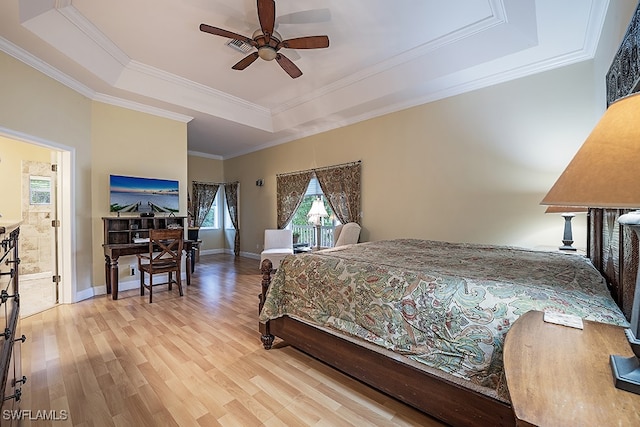 bedroom featuring light wood-type flooring, crown molding, ensuite bath, ceiling fan, and a raised ceiling