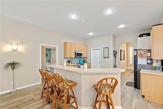 kitchen featuring light brown cabinets, a kitchen bar, light hardwood / wood-style flooring, backsplash, and appliances with stainless steel finishes