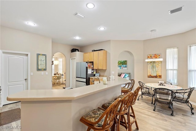 kitchen with sink, light brown cabinets, refrigerator, light wood-type flooring, and kitchen peninsula