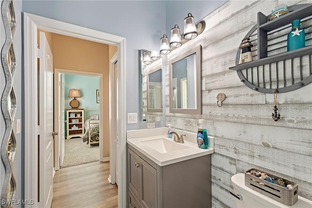 bathroom with toilet, wood walls, hardwood / wood-style floors, and vanity