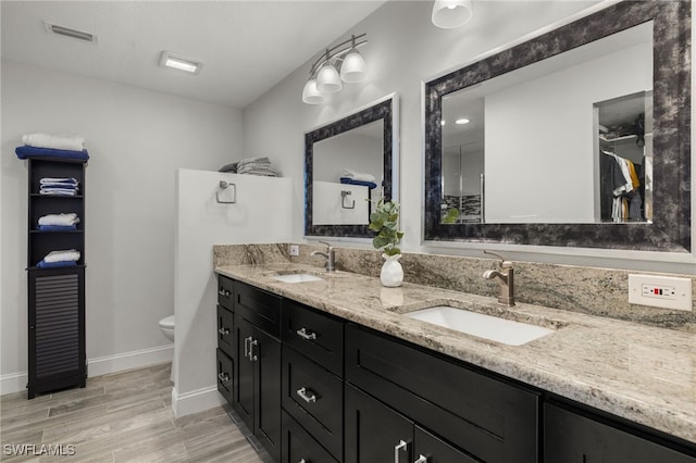 bathroom with toilet, double vanity, visible vents, and a sink