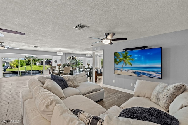 living room featuring a textured ceiling, baseboards, visible vents, ceiling fan, and wood finished floors