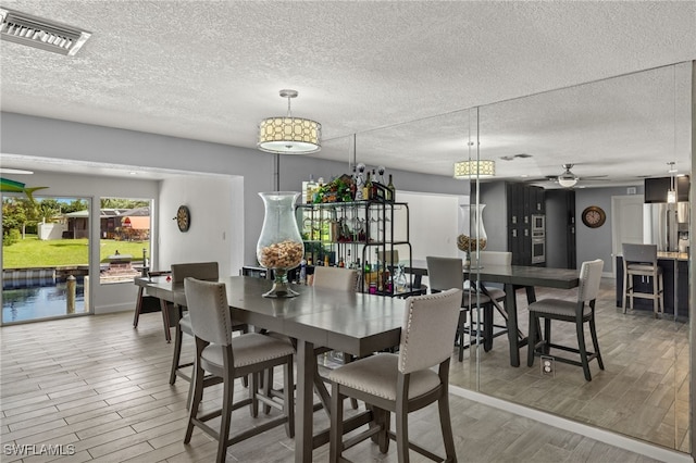 dining space with ceiling fan, light wood-style floors, visible vents, and a textured ceiling