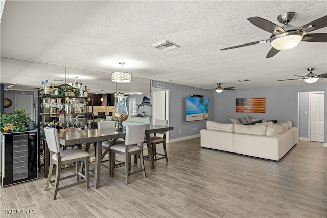 dining space featuring wood finished floors, wine cooler, a textured ceiling, visible vents, and baseboards