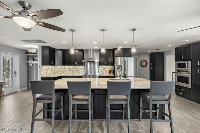 kitchen with a spacious island, wall chimney exhaust hood, appliances with stainless steel finishes, and tasteful backsplash