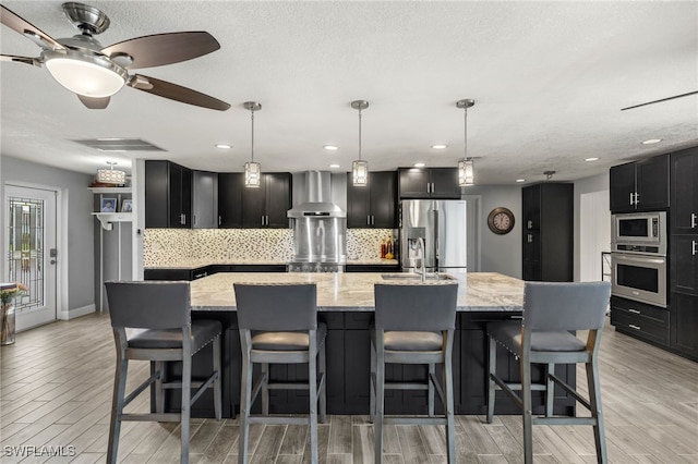 kitchen with backsplash, a large island, appliances with stainless steel finishes, and wall chimney exhaust hood