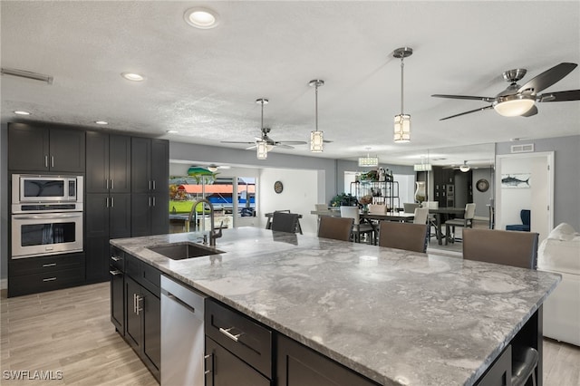 kitchen featuring a sink, stainless steel appliances, light stone counters, ceiling fan, and light wood finished floors