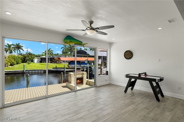 interior space with baseboards, visible vents, wood finished floors, a water view, and a lit fireplace