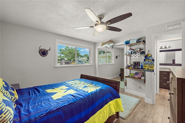 bedroom with a textured ceiling, visible vents, ceiling fan, light wood-style flooring, and baseboards