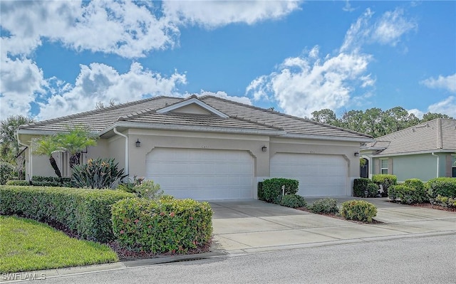 view of front facade featuring a tiled roof, an attached garage, driveway, and stucco siding