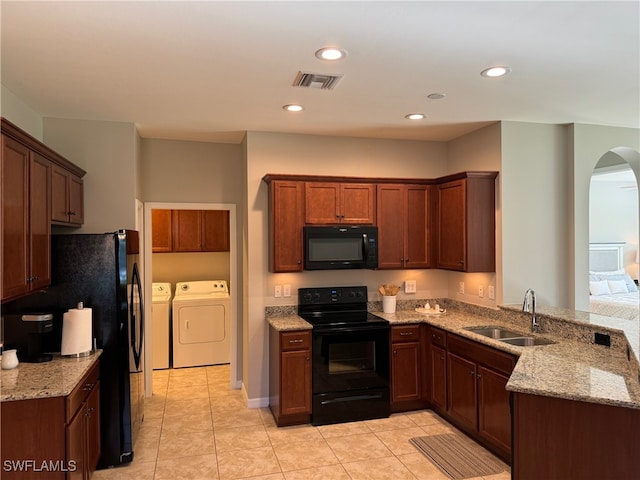 kitchen featuring black appliances, light tile patterned floors, sink, washing machine and dryer, and light stone counters