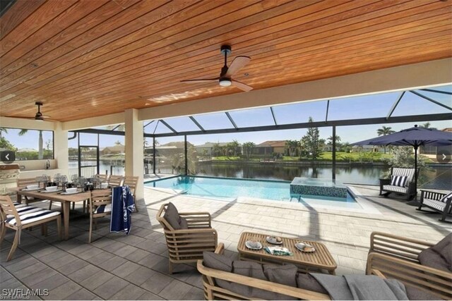 view of pool featuring glass enclosure, a water view, a patio, and ceiling fan