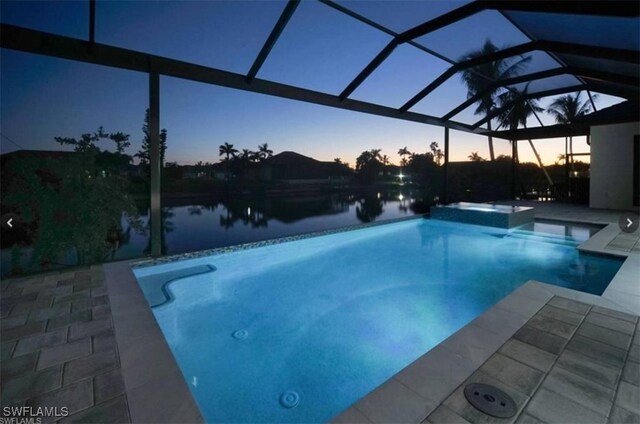 pool at dusk featuring a lanai, a patio, and a water view