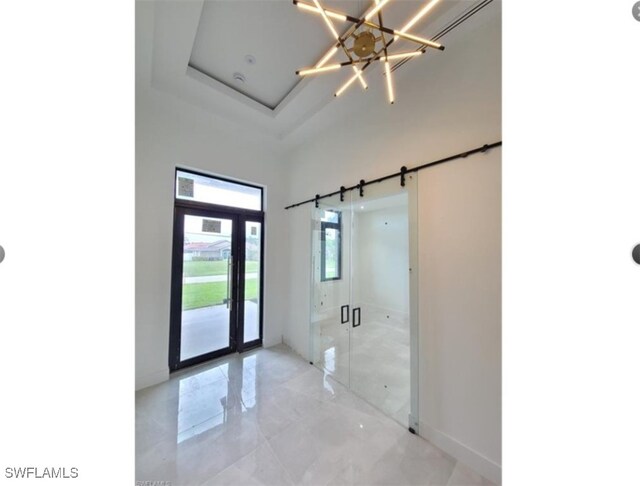 interior space featuring a barn door, a tray ceiling, and a notable chandelier