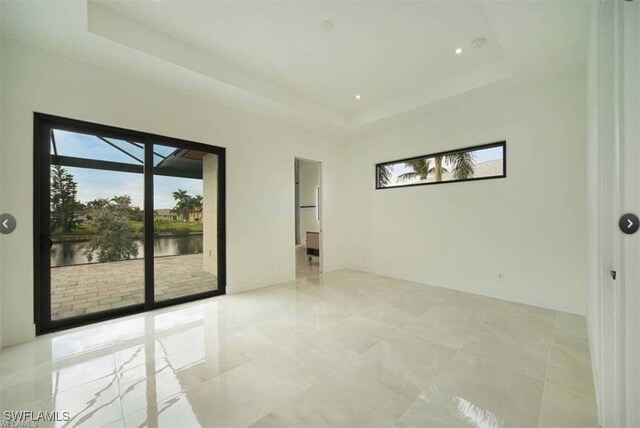 spare room featuring a water view, a tray ceiling, and a healthy amount of sunlight