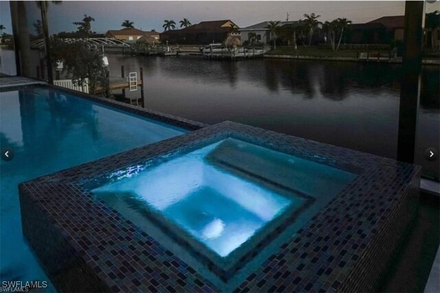 pool at dusk with a water view and an in ground hot tub