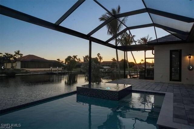 pool at dusk featuring a lanai, a water view, an in ground hot tub, and a patio