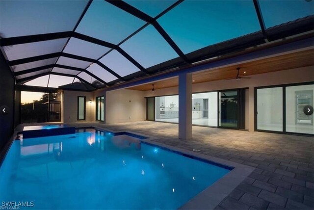 pool at dusk with a lanai, ceiling fan, and a patio