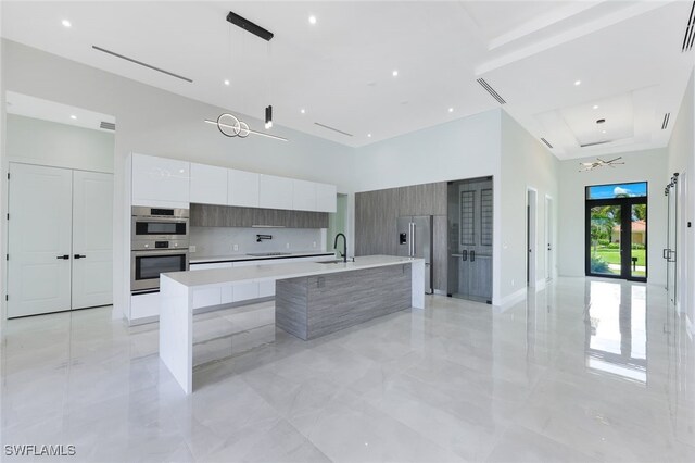 kitchen featuring a kitchen island with sink, pendant lighting, sink, french doors, and white cabinets