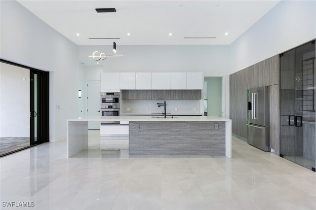 kitchen with pendant lighting, stainless steel appliances, white cabinets, and a kitchen island with sink