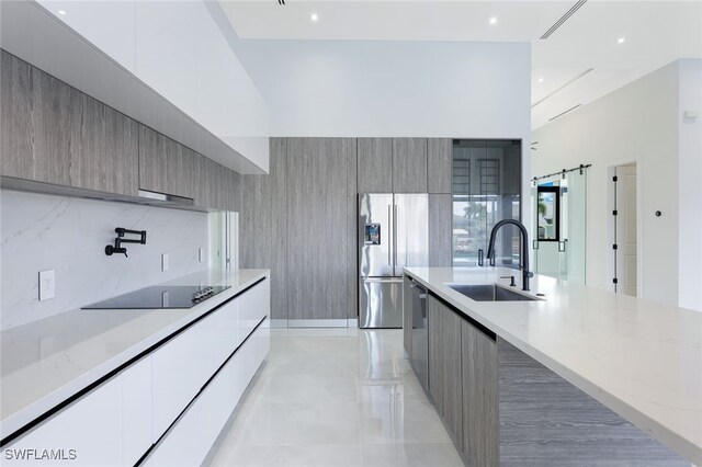 kitchen with a barn door, light stone counters, stainless steel appliances, sink, and decorative backsplash