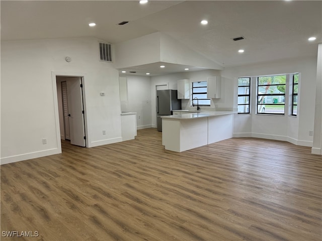 kitchen with white cabinets, hardwood / wood-style flooring, kitchen peninsula, and stainless steel refrigerator