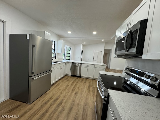 kitchen featuring appliances with stainless steel finishes, white cabinetry, lofted ceiling, light hardwood / wood-style flooring, and sink