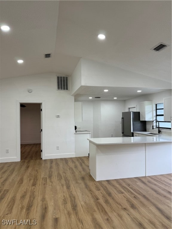 kitchen featuring stainless steel fridge, white cabinetry, vaulted ceiling, hardwood / wood-style flooring, and sink