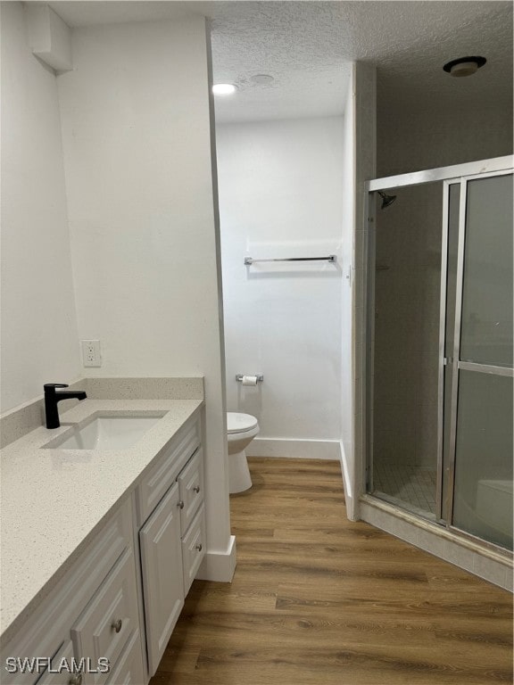 bathroom featuring a textured ceiling, hardwood / wood-style flooring, a shower with door, vanity, and toilet