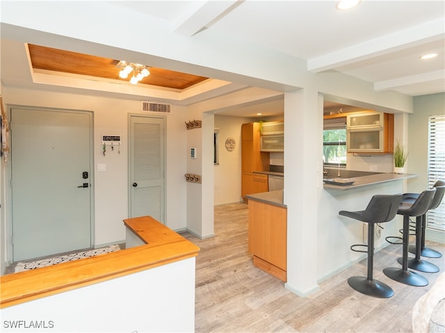 kitchen with a kitchen bar, a raised ceiling, kitchen peninsula, and light hardwood / wood-style flooring